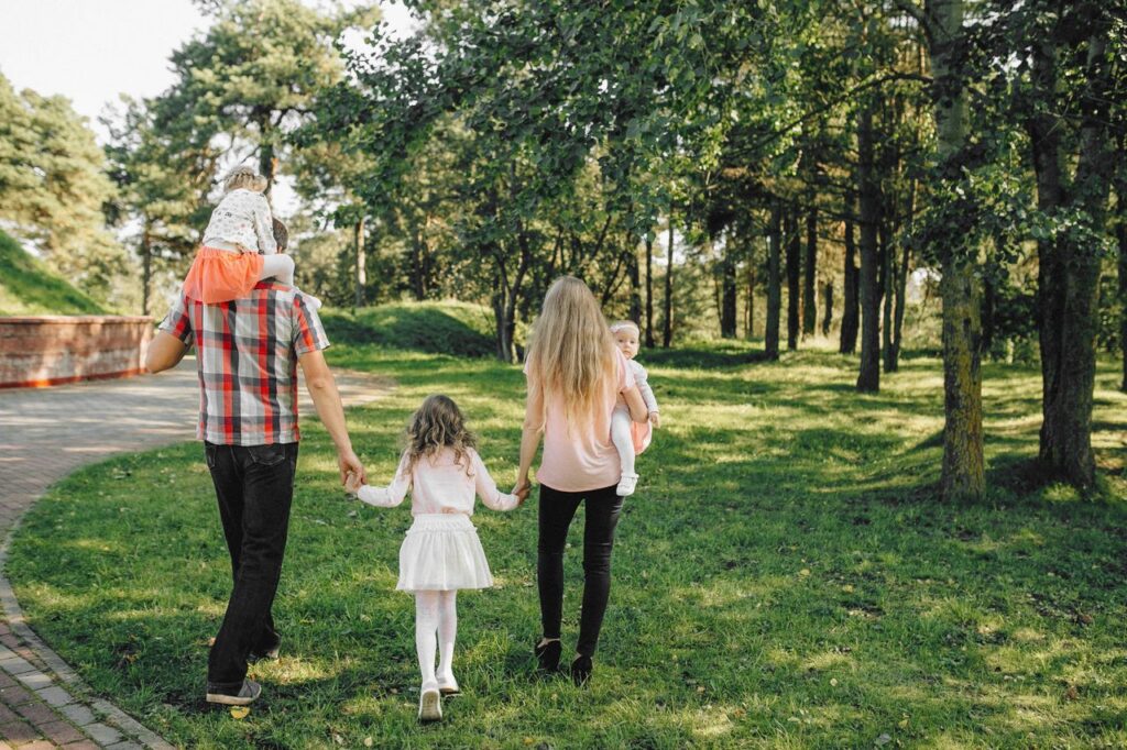 A family enjoying a walk under dappled sunlight in a lush green park.