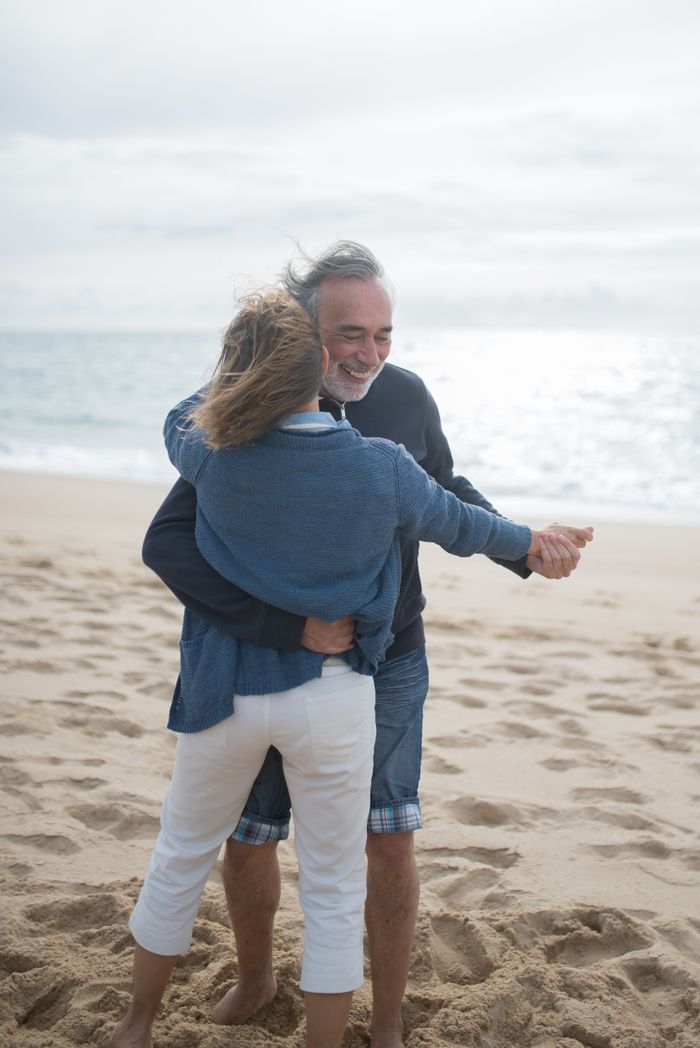 Elderly couple dances joyfully on a serene Portuguese beach, capturing a moment of happiness and togetherness.