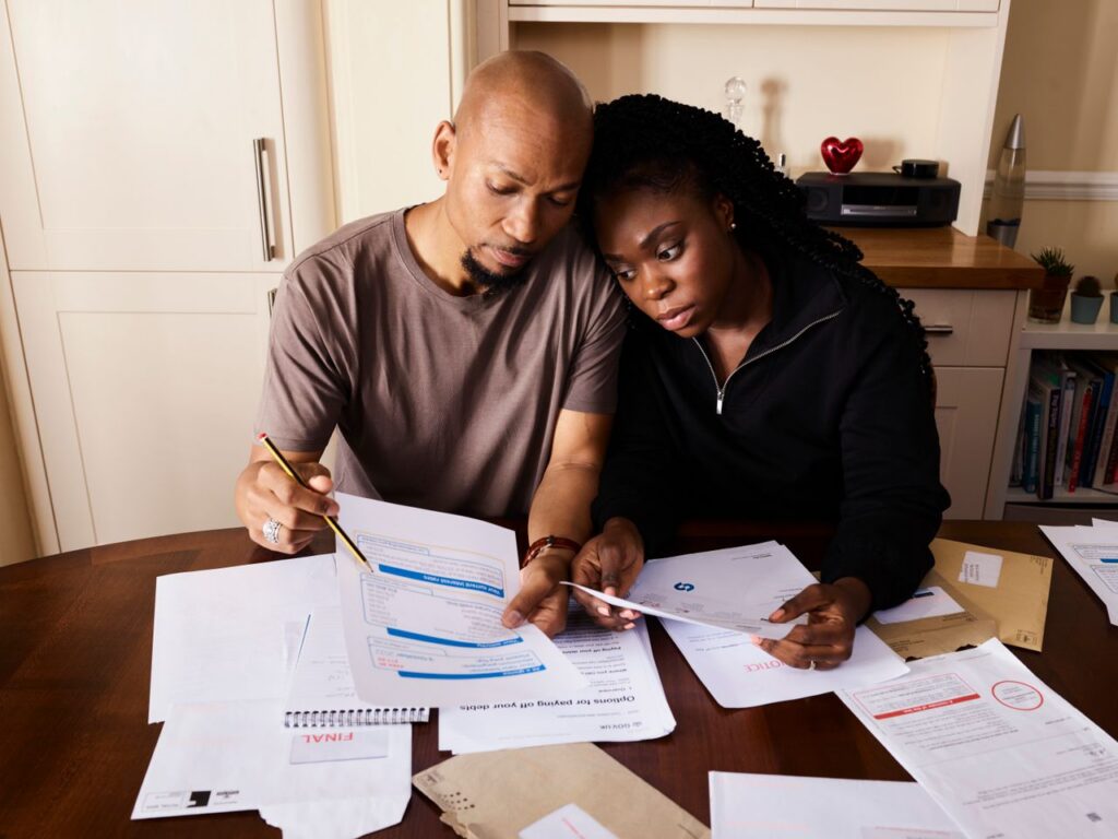 A couple sitting at a table reviewing financial documents, highlighting domestic budgeting.